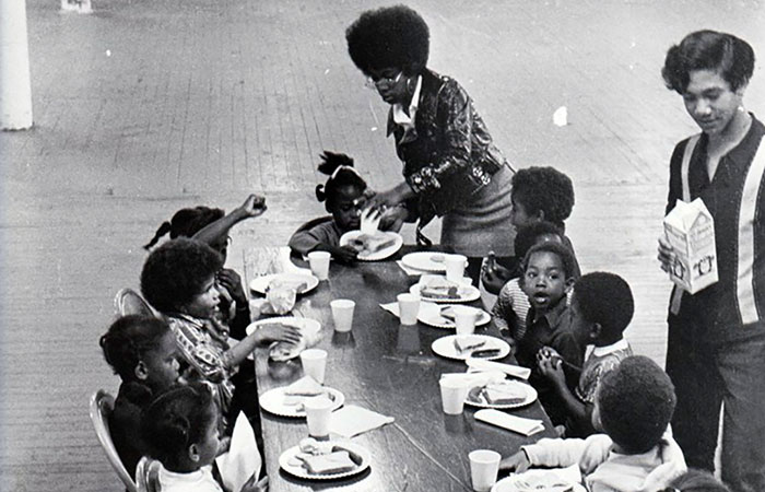 Two women serving breakfast to group of students before school