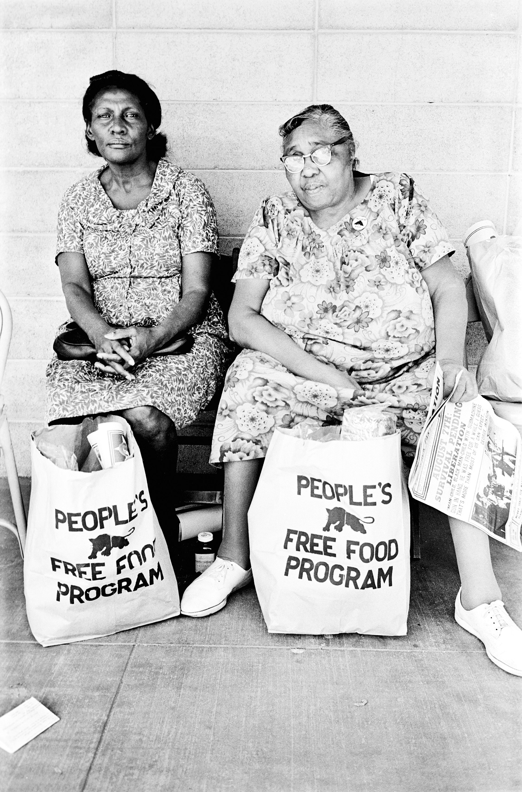 Two women with free groceries sitting on a bench.